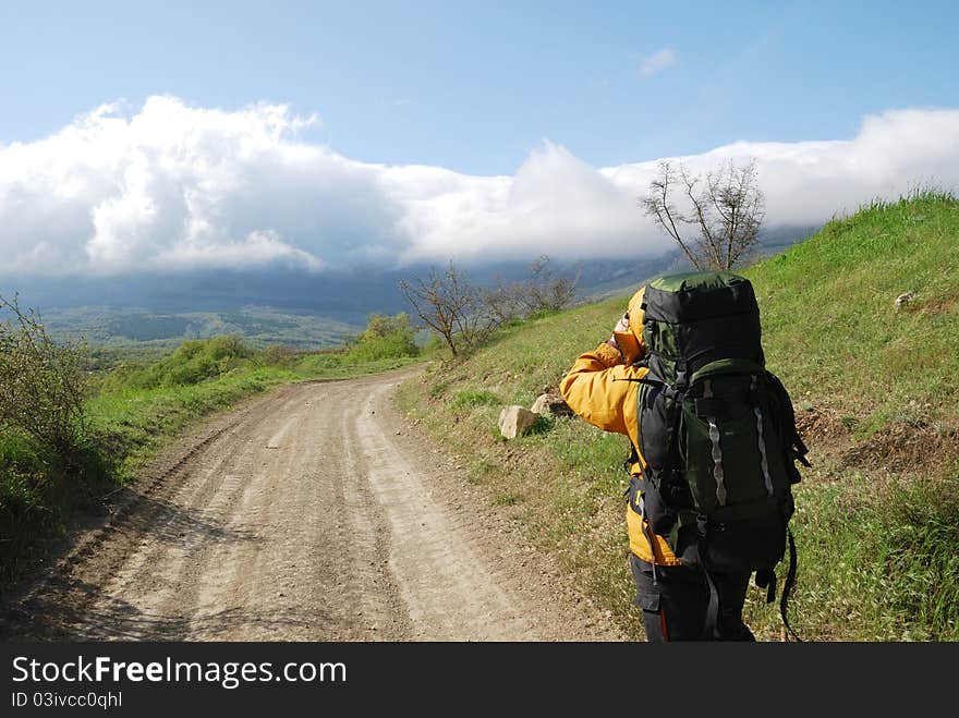 Hiker is shooting a landscape by video camera. He is standing on the natural road. He is carrying a large rucksack. Hiker is shooting a landscape by video camera. He is standing on the natural road. He is carrying a large rucksack.