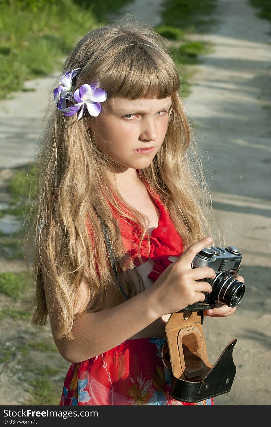 The girl the teenager with a fair hair costs in rural street with the camera in a hand. The girl the teenager with a fair hair costs in rural street with the camera in a hand