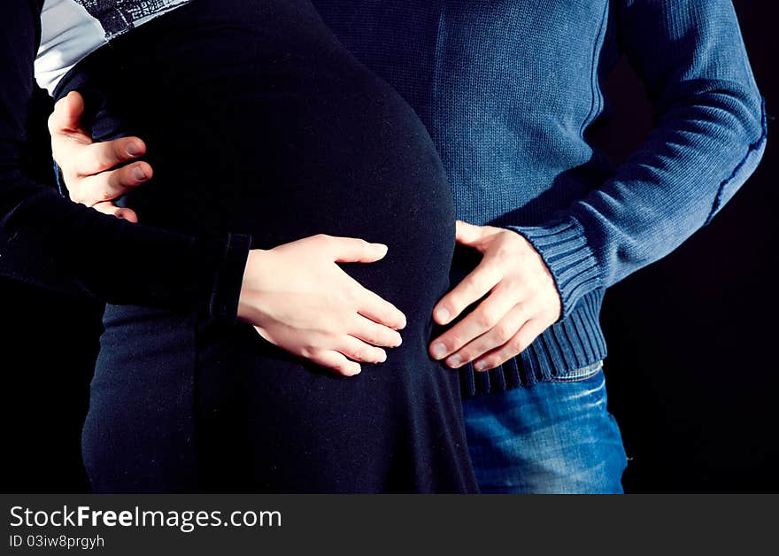 Pregnant woman and her husband caressing her belly with dark background