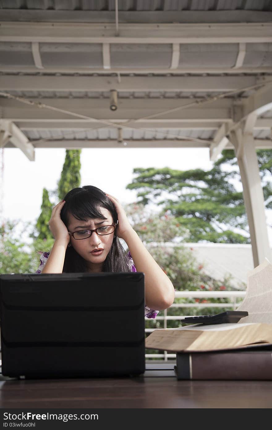 Stressed asian woman with her laptop and book. Stressed asian woman with her laptop and book