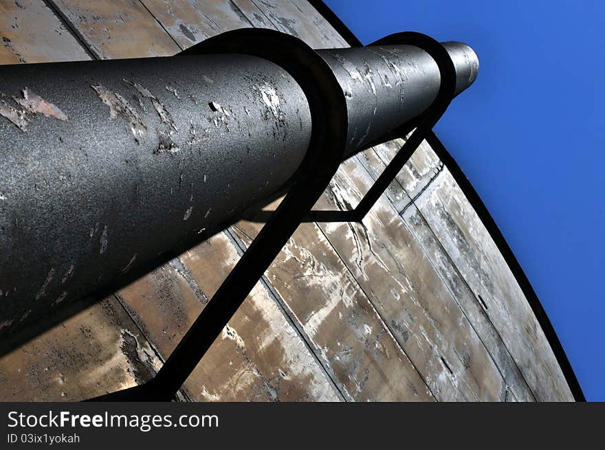 Large iron pipe strapped to side of community water tank with blue sky above. Large iron pipe strapped to side of community water tank with blue sky above