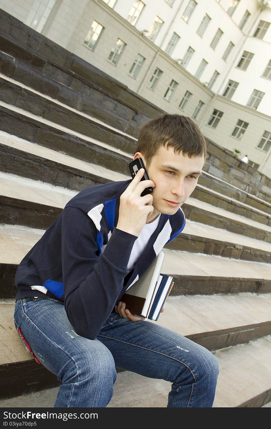 Close-up of a modern student talking on a cell phone on campus. In the hand holding books. Close-up of a modern student talking on a cell phone on campus. In the hand holding books