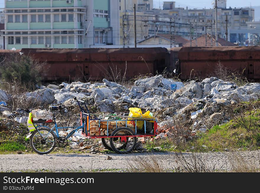 Bicycle on 3 wheels of a homeless individual full with food. Dirt, old train and buildings in the background. Bicycle on 3 wheels of a homeless individual full with food. Dirt, old train and buildings in the background