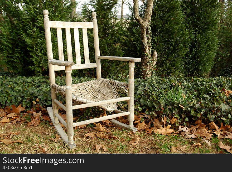 Old weathered rocking chair in yard surrounded by greens, ivy and old leaves. Old weathered rocking chair in yard surrounded by greens, ivy and old leaves
