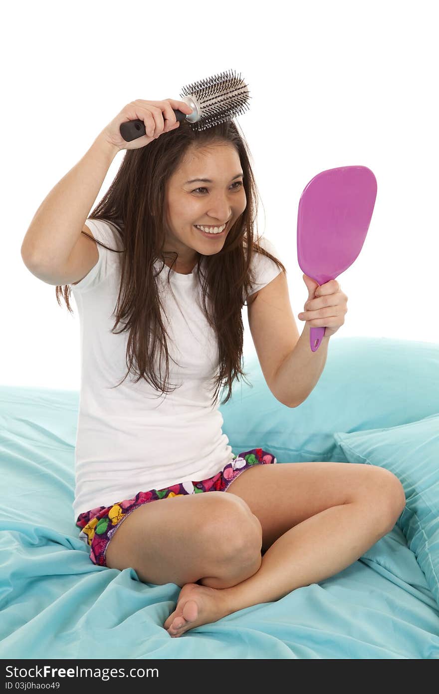 A woman sitting on her bed looking in her mirror brushing her hair. A woman sitting on her bed looking in her mirror brushing her hair.