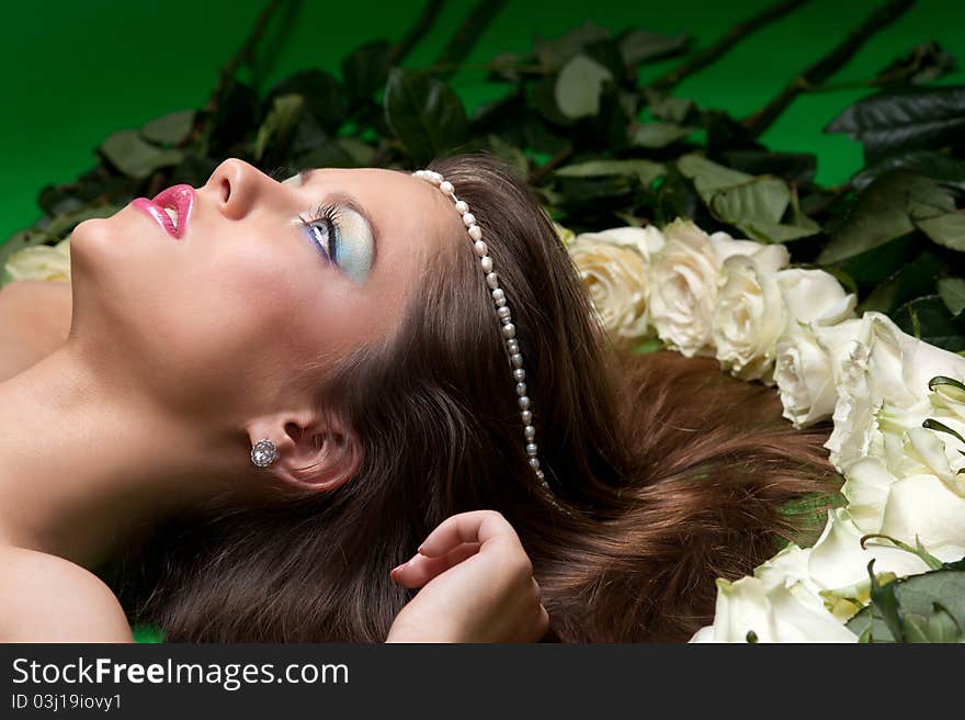 Young girl lay among the flowers of roses on a green background