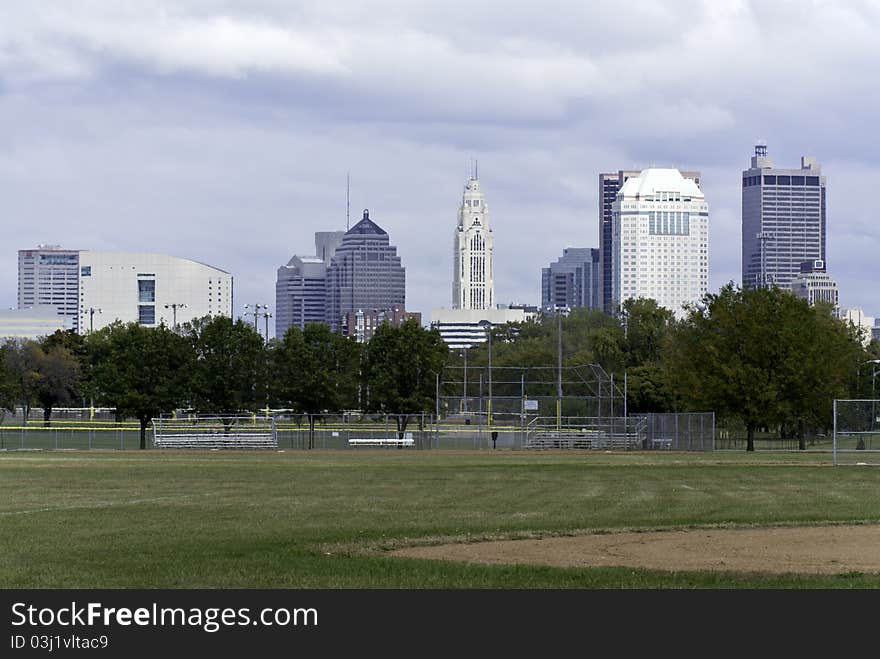 A view of a city scape as seen with a baseball field in the foreground and an overcast sky in the background. A view of a city scape as seen with a baseball field in the foreground and an overcast sky in the background.