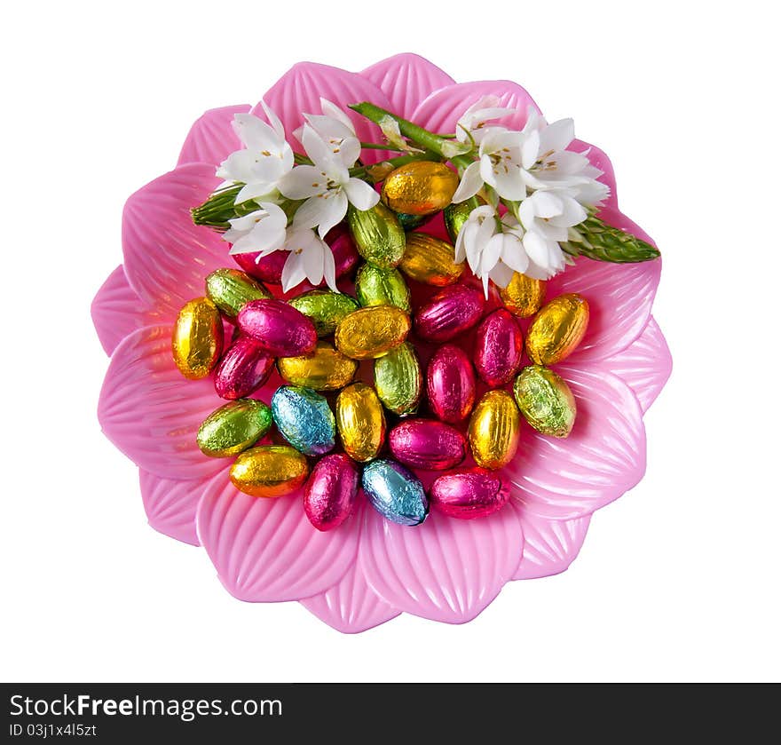 White beautiful decorative flowers on a dish with colorful foiled chocolates isolated over white background. White beautiful decorative flowers on a dish with colorful foiled chocolates isolated over white background