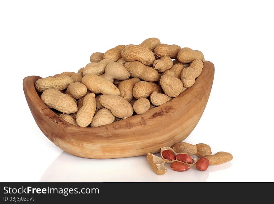 Peanut monkey nuts in an olive wood bowl and scattered isolated over white background. Peanut monkey nuts in an olive wood bowl and scattered isolated over white background.