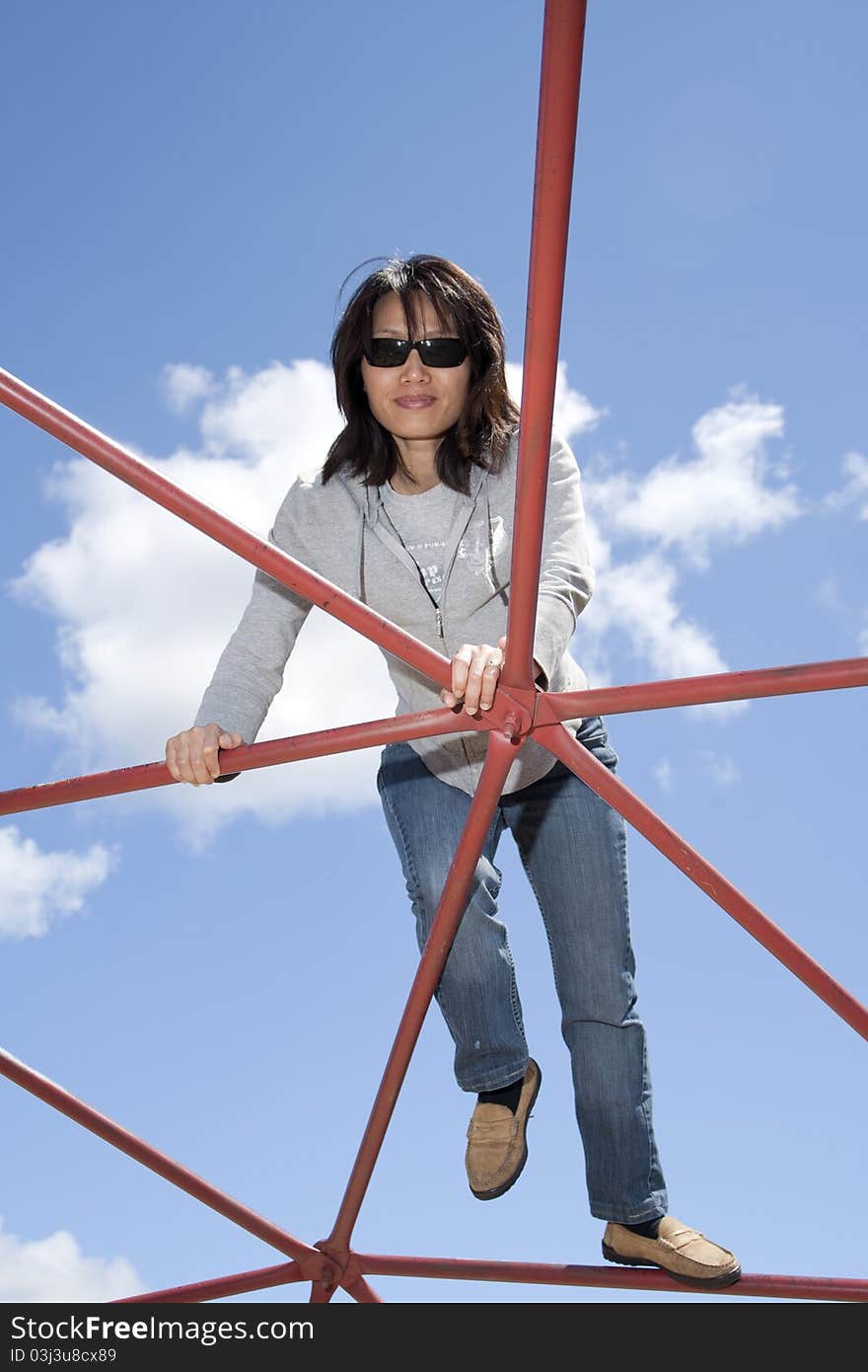 A pretty woman climbs up on a piece of playground equipment on a sunny day. A pretty woman climbs up on a piece of playground equipment on a sunny day.