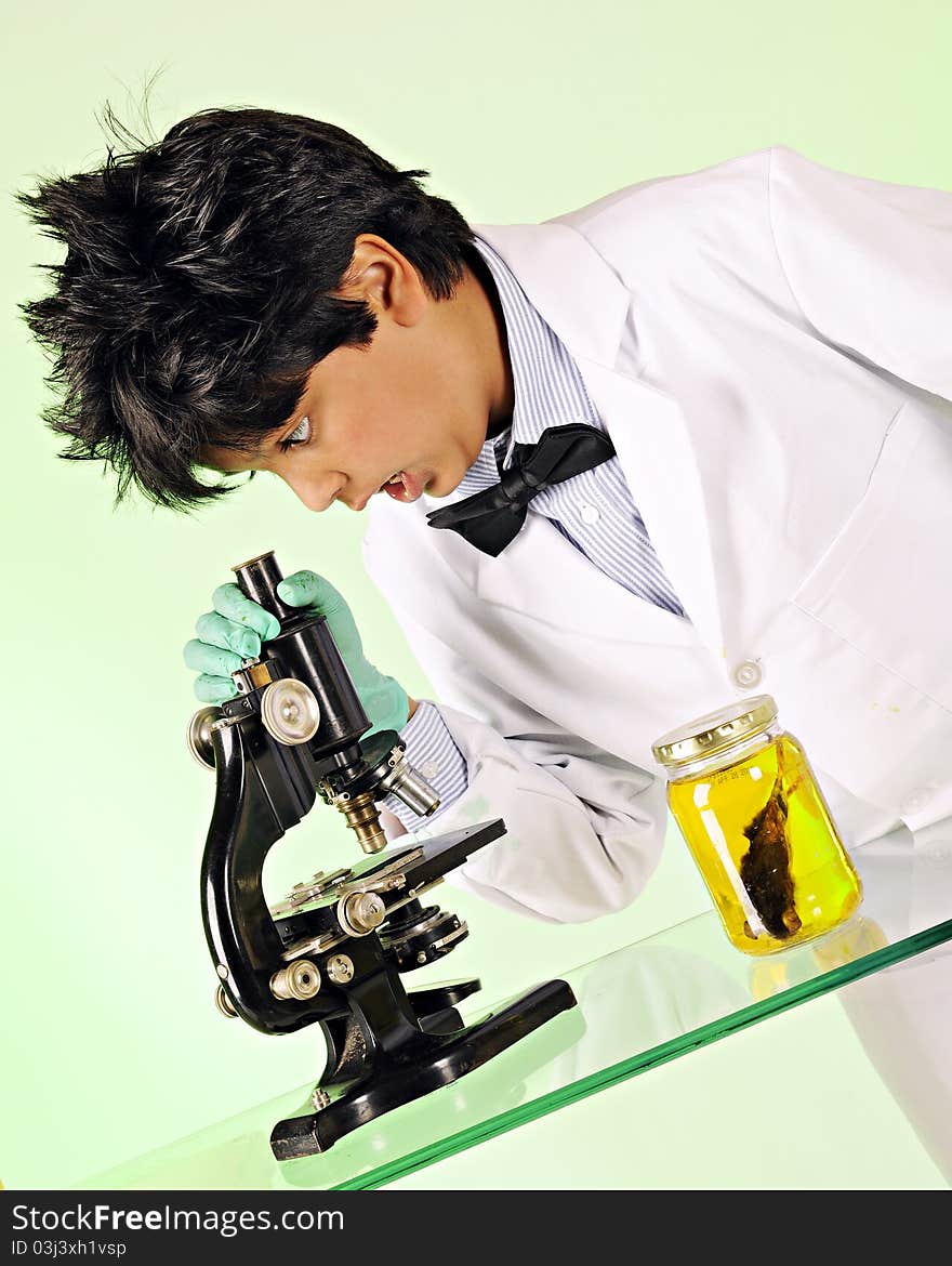 A young mad scientist shocked at what he sees through a microscope. A mouse specimen sits in a bottle nearby. A young mad scientist shocked at what he sees through a microscope. A mouse specimen sits in a bottle nearby.