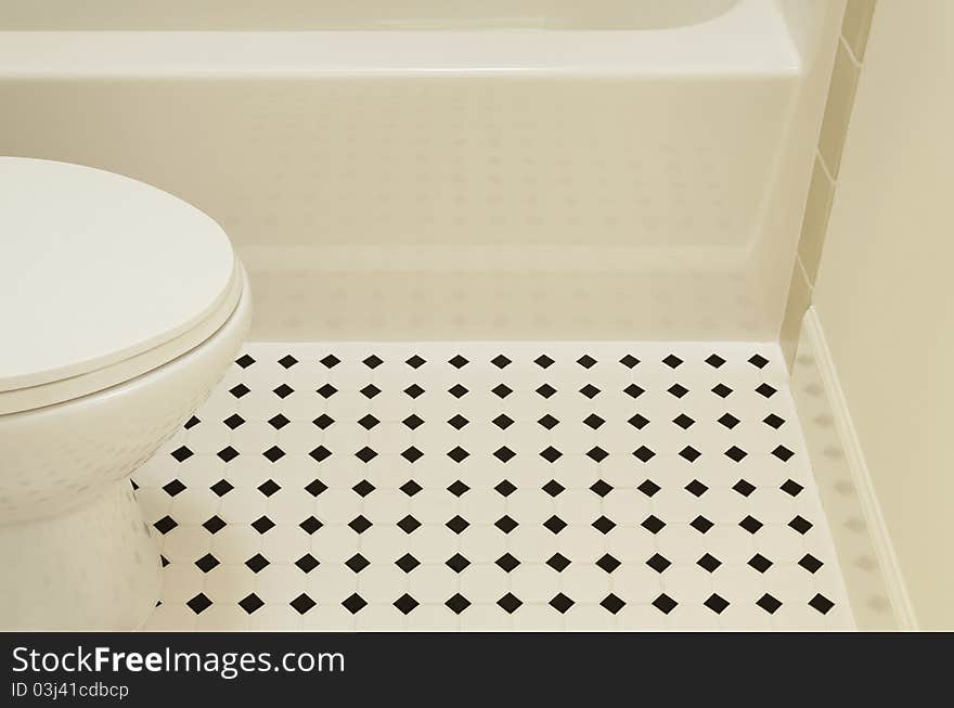 A white acrylic bathtub and porcelain toilet of a bathroom are sitting on a diamond patterned vinyl flooring in a bathroom. Horizontal shot. A white acrylic bathtub and porcelain toilet of a bathroom are sitting on a diamond patterned vinyl flooring in a bathroom. Horizontal shot.