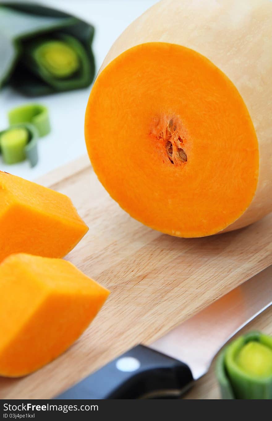 Cut pumpkin on wooden board with leek on background