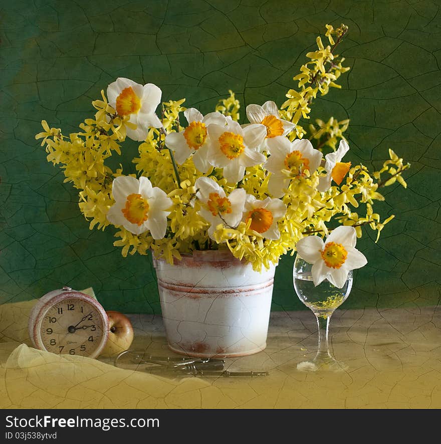 A bouquet of narcissuses is in a bucket, alongside clock and apple