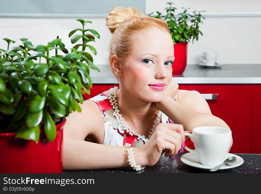 Young beautiful girl wearing white and pink dress with cup of morning coffee in interior of red modern kitchen. Young beautiful girl wearing white and pink dress with cup of morning coffee in interior of red modern kitchen