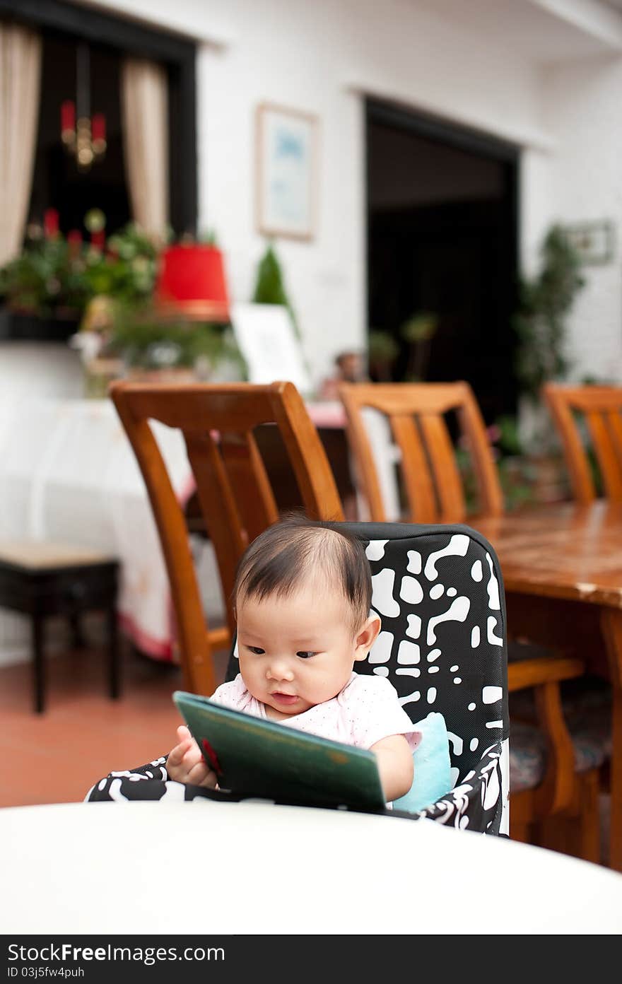 7 month old Asian baby girl reading lunch menu, sitting on a high chair