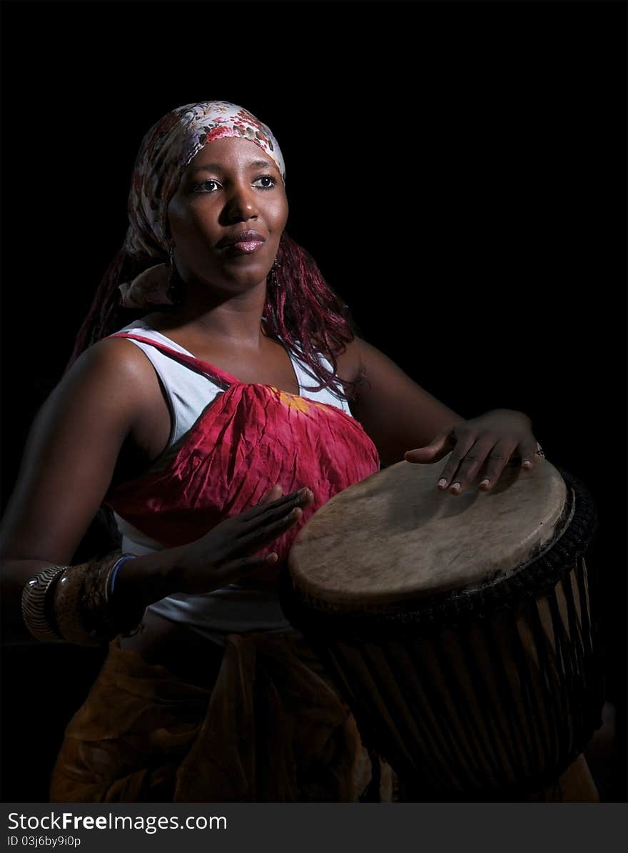 An african drummer plays a djembe drum set against a dark background. An african drummer plays a djembe drum set against a dark background