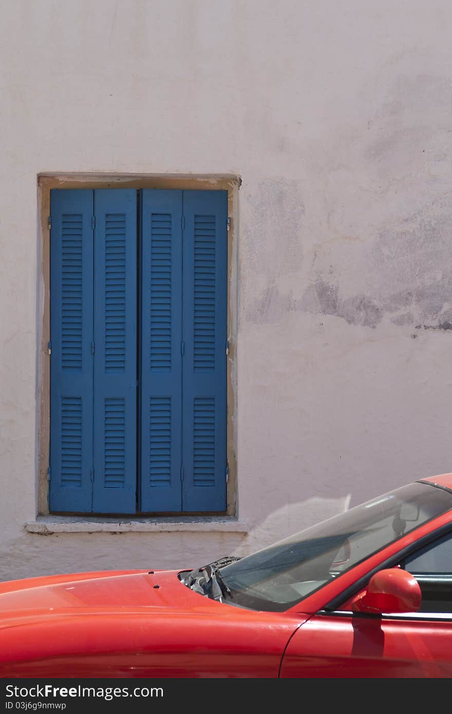 A sunlit bright red automobile constrasts with shaded deep blue shutters. A sunlit bright red automobile constrasts with shaded deep blue shutters