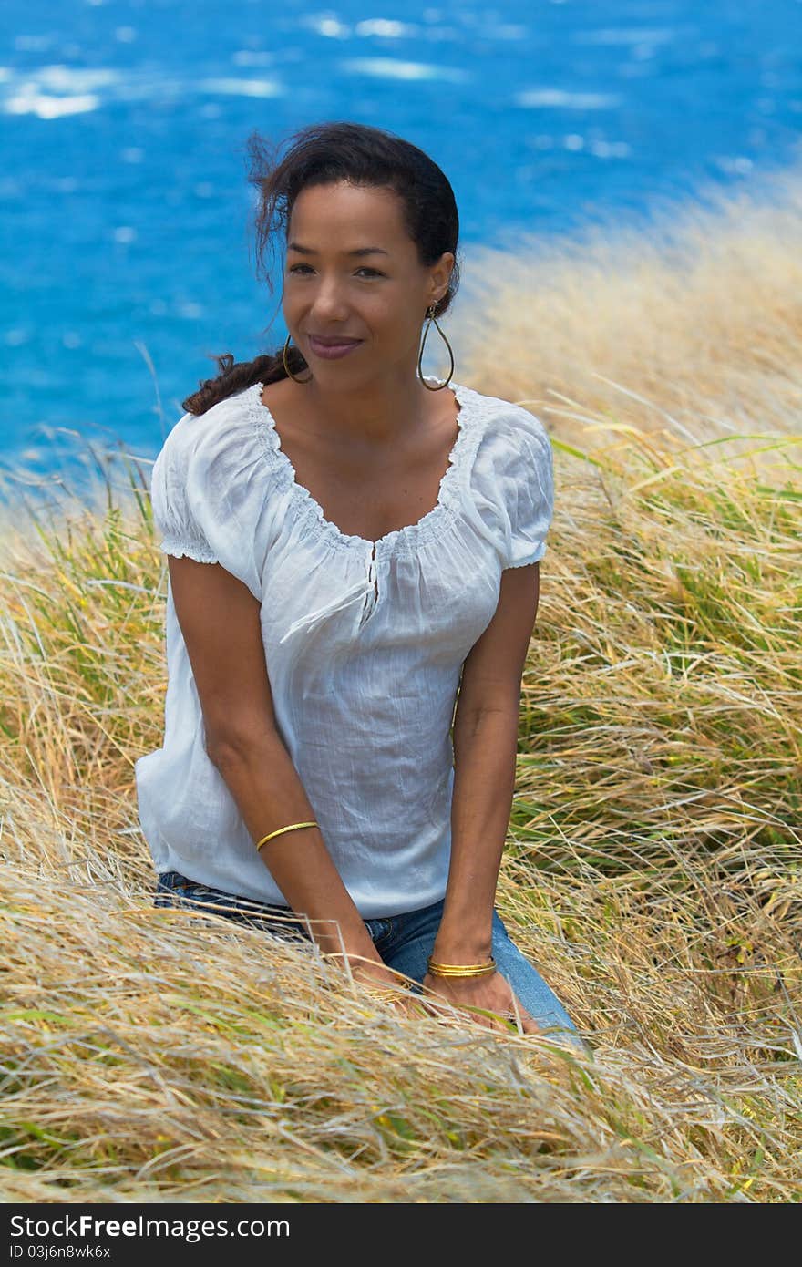 An exotic Hawaiian woman sits in the tall grass on a cliffside overlooking the ocean in Maui, Hawaii. Vertical image orientation. An exotic Hawaiian woman sits in the tall grass on a cliffside overlooking the ocean in Maui, Hawaii. Vertical image orientation.