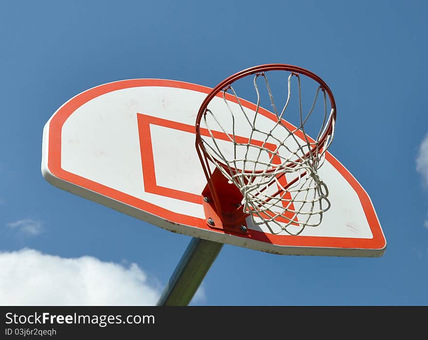 Basketball hoop with white and red backboard, against a blue sky background with a tuft of clouds