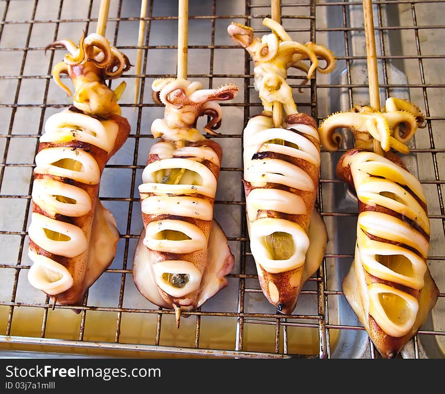 Skewered squid on wooden sticks grilled tentacles , market Thailand