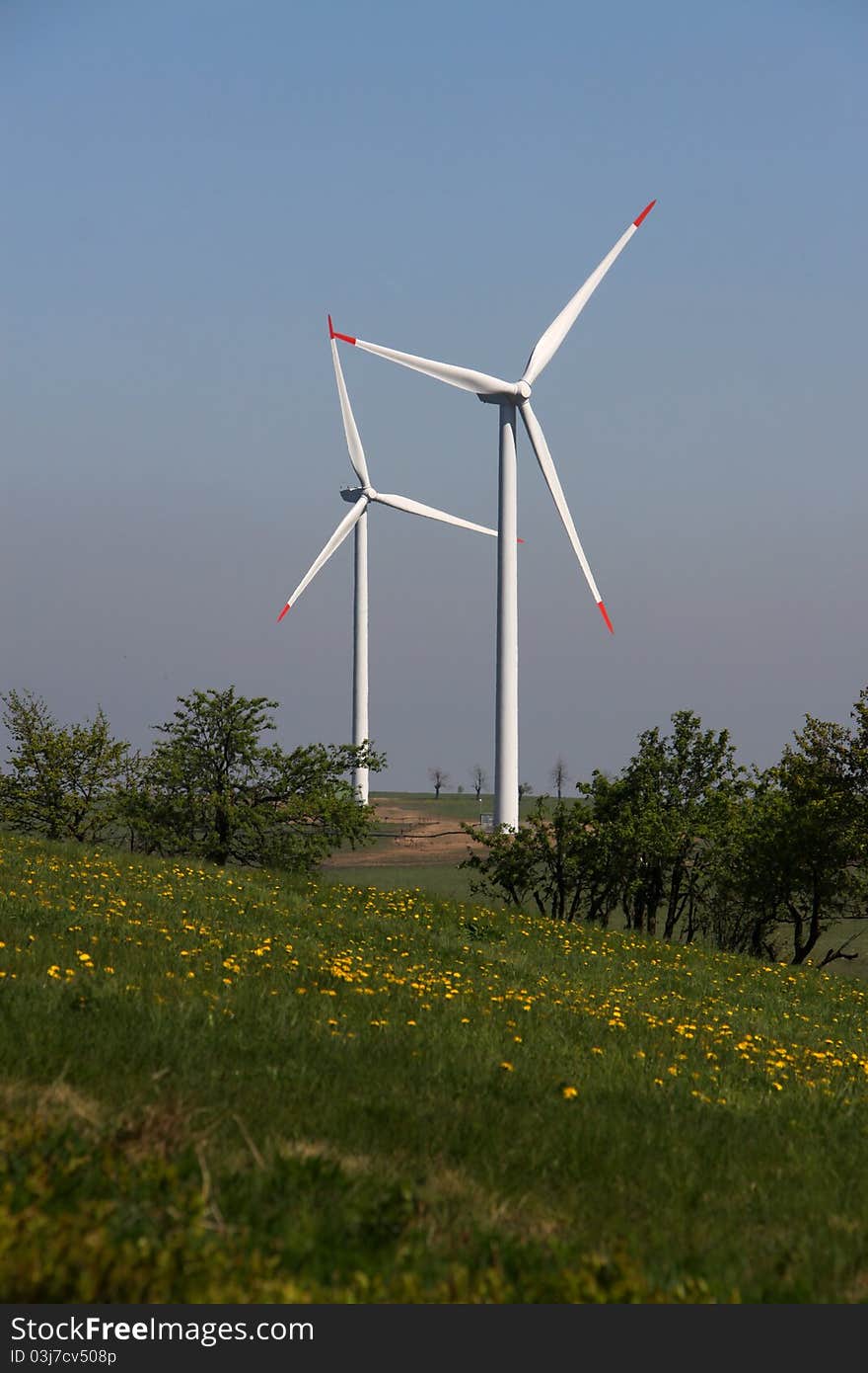 Two wind power plants over the field with dandelions. Two wind power plants over the field with dandelions