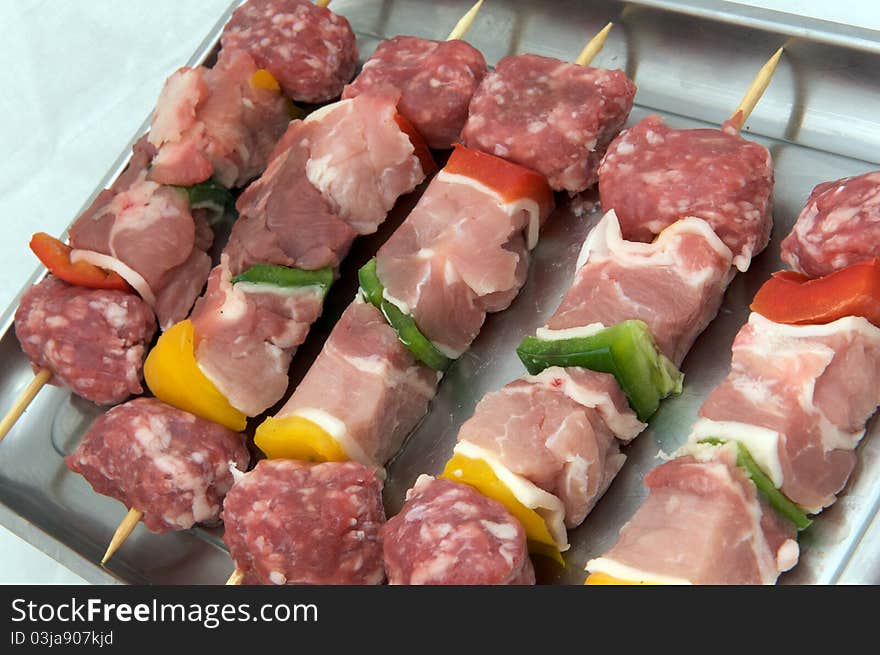 Skewers of raw meat and peppers, white background