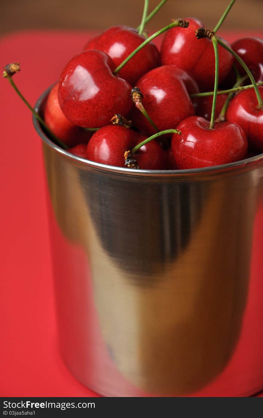 Fresh cherries in a metal cup on a red background. Fresh cherries in a metal cup on a red background.