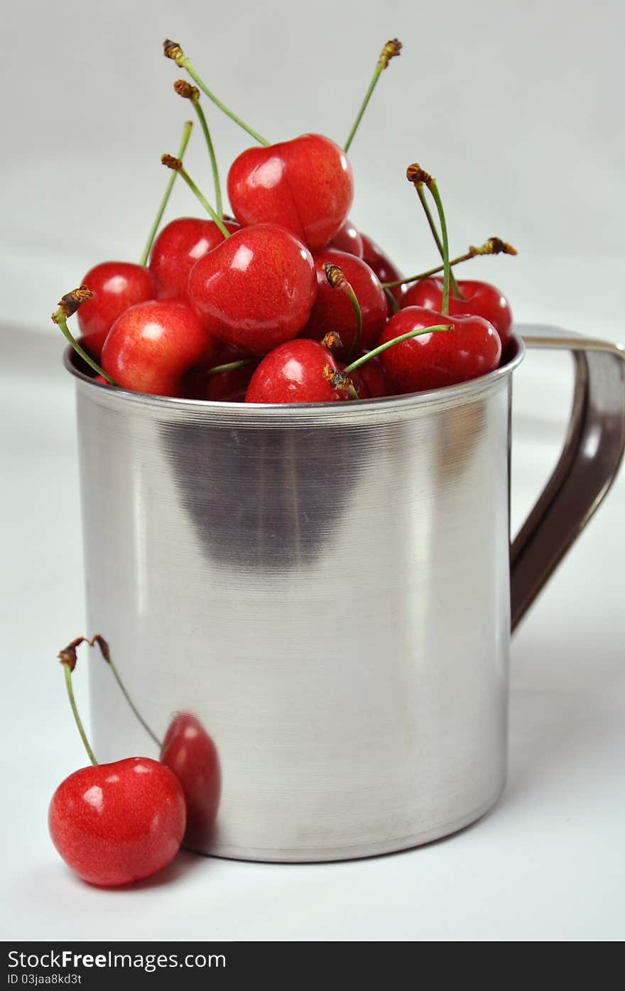 Fresh cherries in a metal cup on a white background. Fresh cherries in a metal cup on a white background.