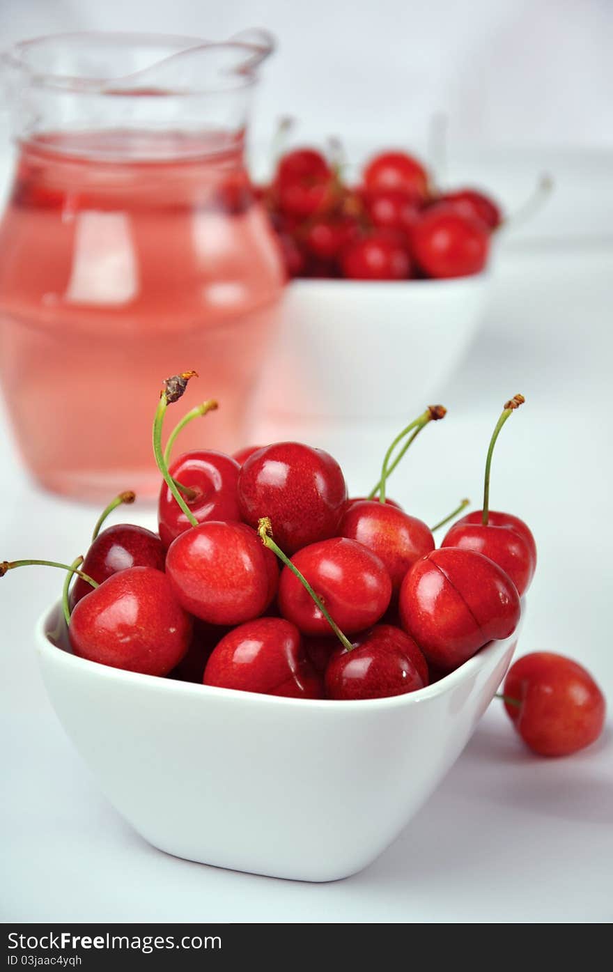 Fresh cherries in white bowls and a jug on a white background. Fresh cherries in white bowls and a jug on a white background.