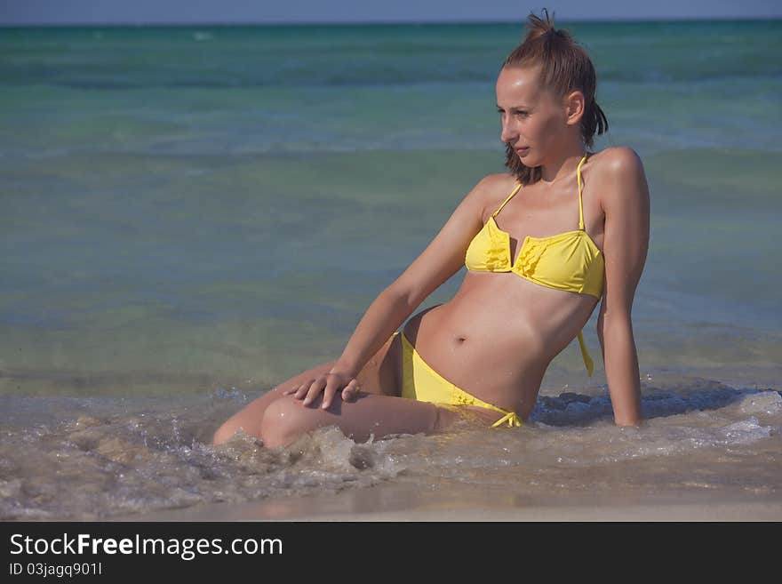 Woman in yellow bikini resting at the beach in ocean waves. Woman in yellow bikini resting at the beach in ocean waves