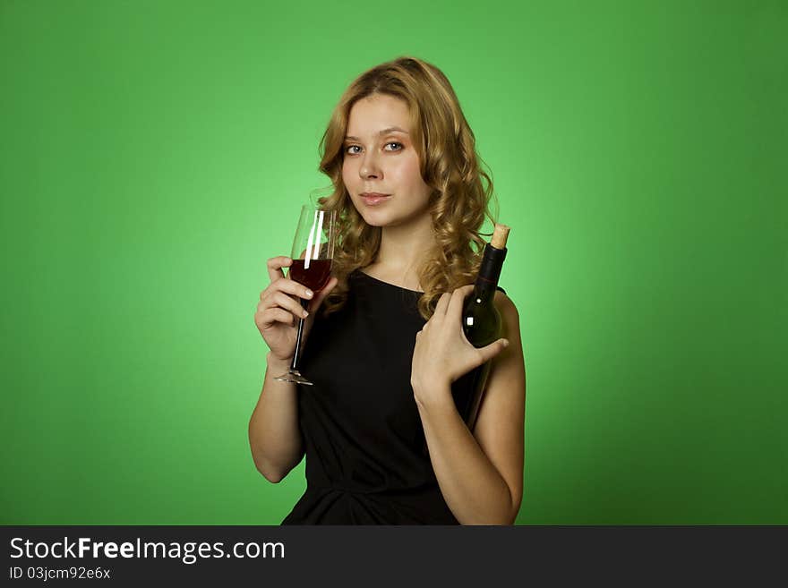 Close-up of an attractive woman on a green background in one hand and bottle in another glass of red wine. Close-up of an attractive woman on a green background in one hand and bottle in another glass of red wine