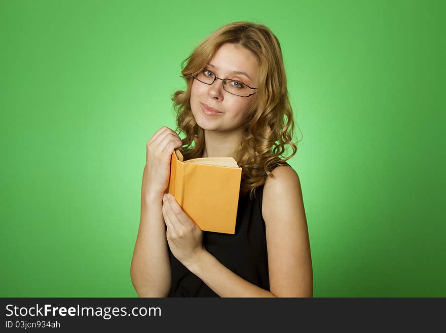 Close-up on a green background attractive girl with glasses and a little yellow book. Close-up on a green background attractive girl with glasses and a little yellow book