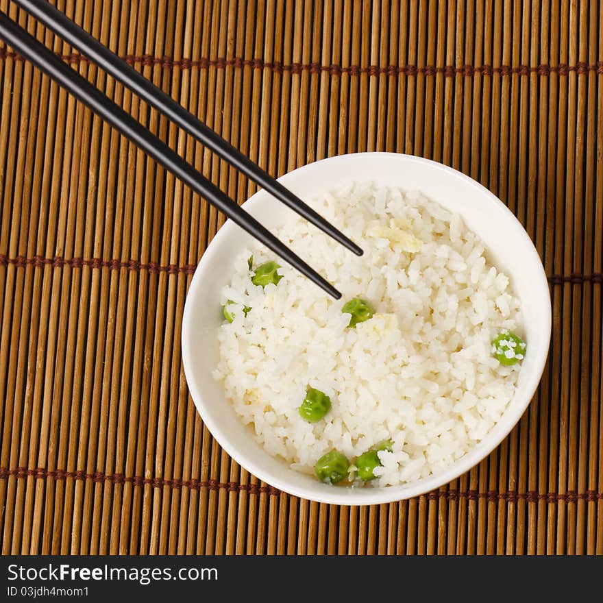 A bowl of egg fried rice with a pair of chopsticks in shoot