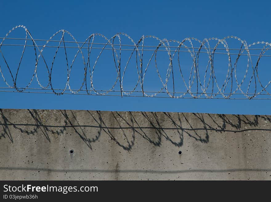 A security barrier made from spiralled razor wire and a concrete wall with a blue sky in the background. A security barrier made from spiralled razor wire and a concrete wall with a blue sky in the background.