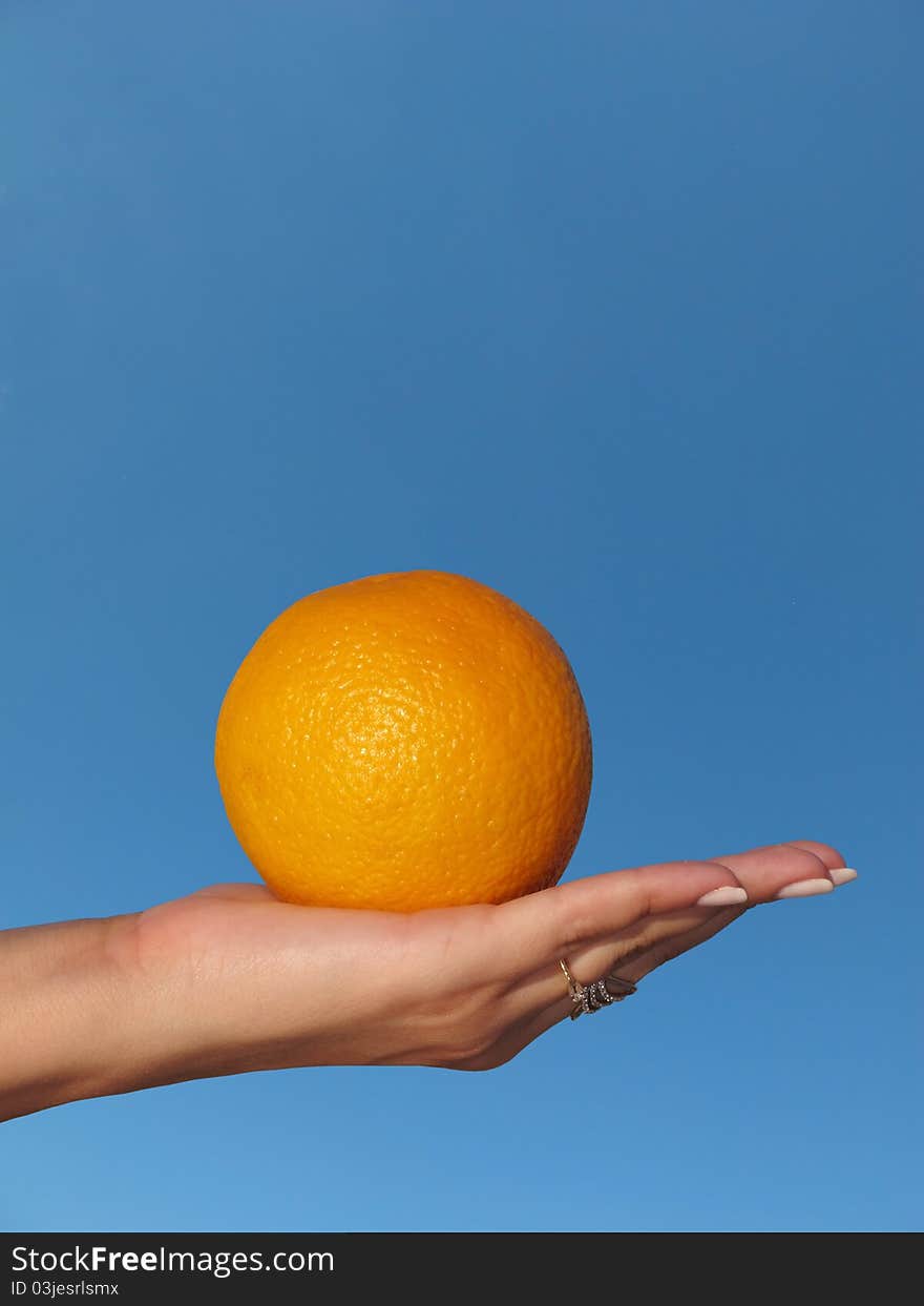 Orange in a female hand against the blue sky