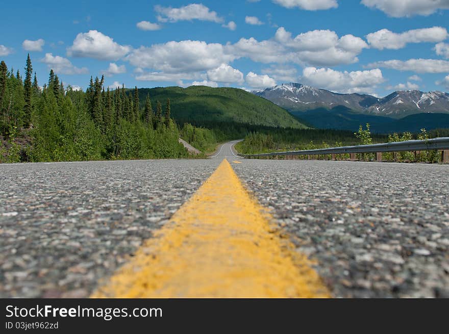 A bright yellow line provides high contrast against the lush green vegetation and perfect blue sky while riding into the Yukon from Alaska on hwy 4. A bright yellow line provides high contrast against the lush green vegetation and perfect blue sky while riding into the Yukon from Alaska on hwy 4