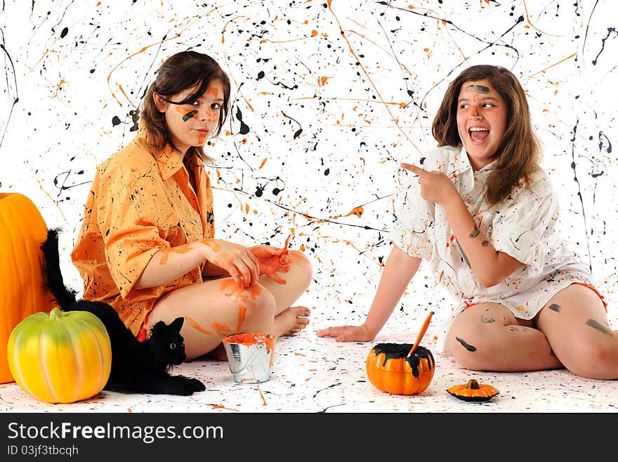 A teen and preteen making a halloween mess with black and orange pain. A black cat and pumpkins nearby. A teen and preteen making a halloween mess with black and orange pain. A black cat and pumpkins nearby.