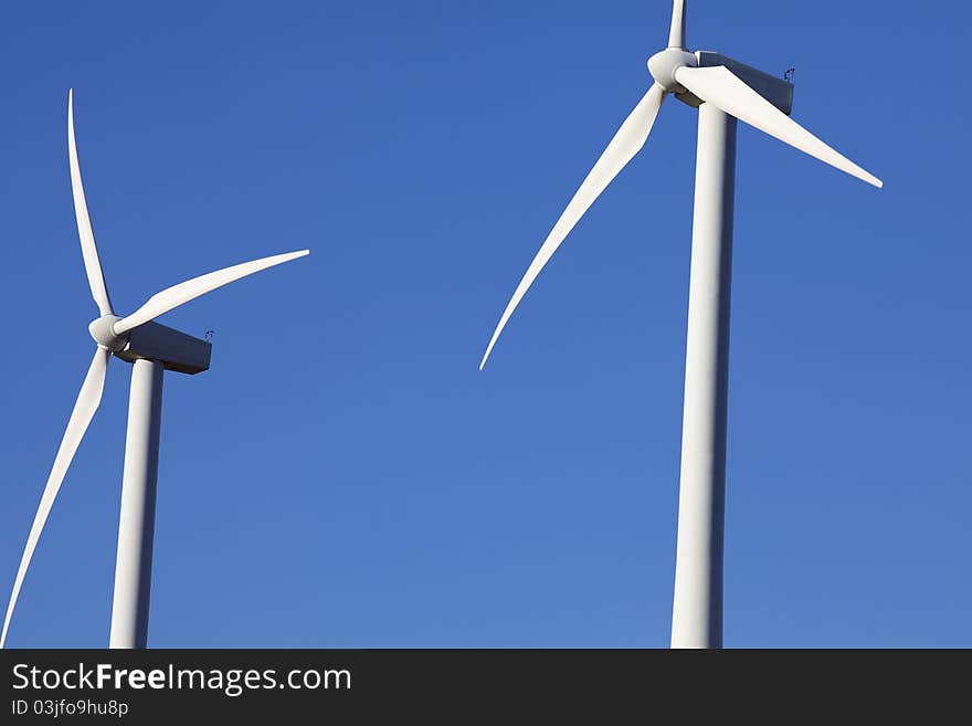 Two Wind Turbines for alternative energy production against clear blue sky. Two Wind Turbines for alternative energy production against clear blue sky