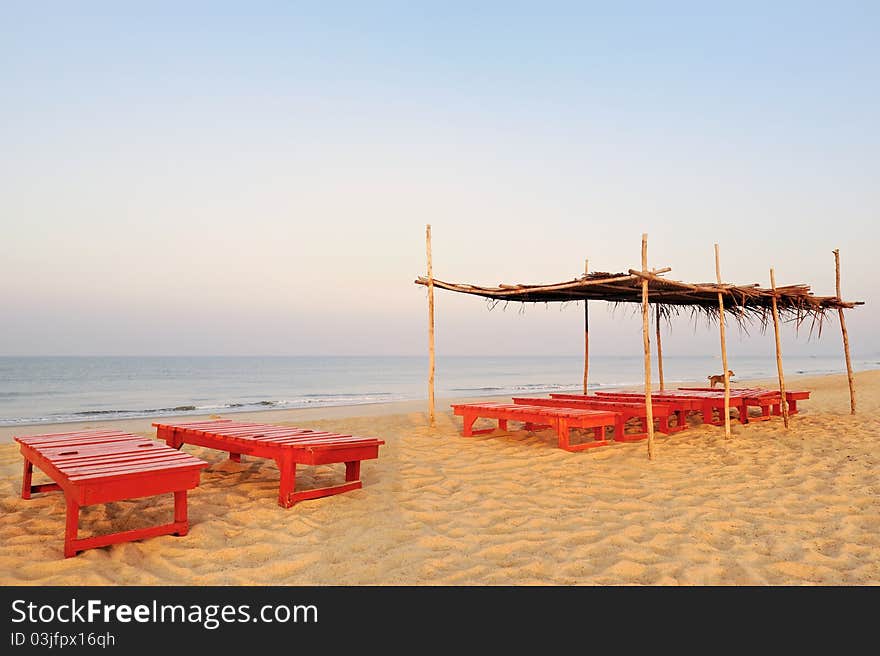 Exotic lean-to of palm leaves and red deck-chairs on tropical beach. Exotic lean-to of palm leaves and red deck-chairs on tropical beach