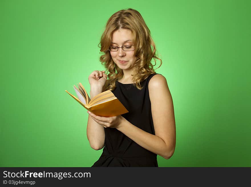 Close-up on a green background attractive girl with glasses and a little yellow book. Close-up on a green background attractive girl with glasses and a little yellow book