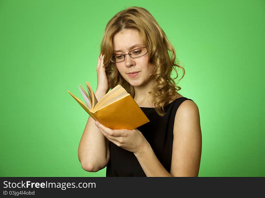 Close-up on a green background attractive girl with glasses and a little yellow book. Close-up on a green background attractive girl with glasses and a little yellow book