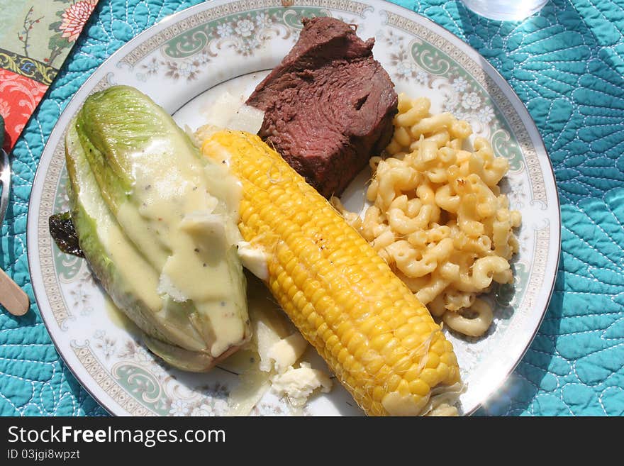 Plate of food with beef, corn, grilled romaine and macaroni and cheese. Plate of food with beef, corn, grilled romaine and macaroni and cheese.