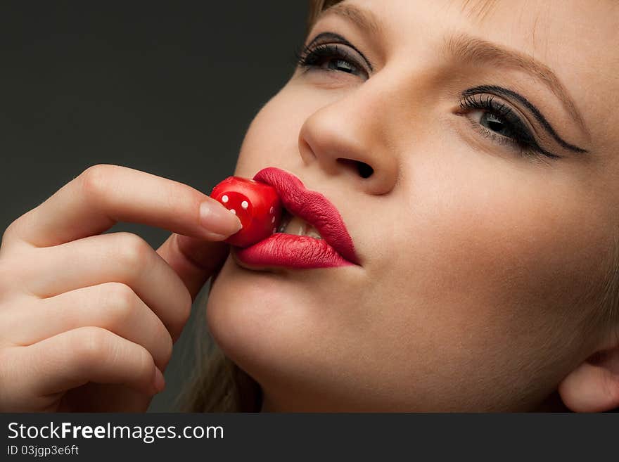 Portrait of a woman's face holding in mouth a red dice, against a white background. Portrait of a woman's face holding in mouth a red dice, against a white background.