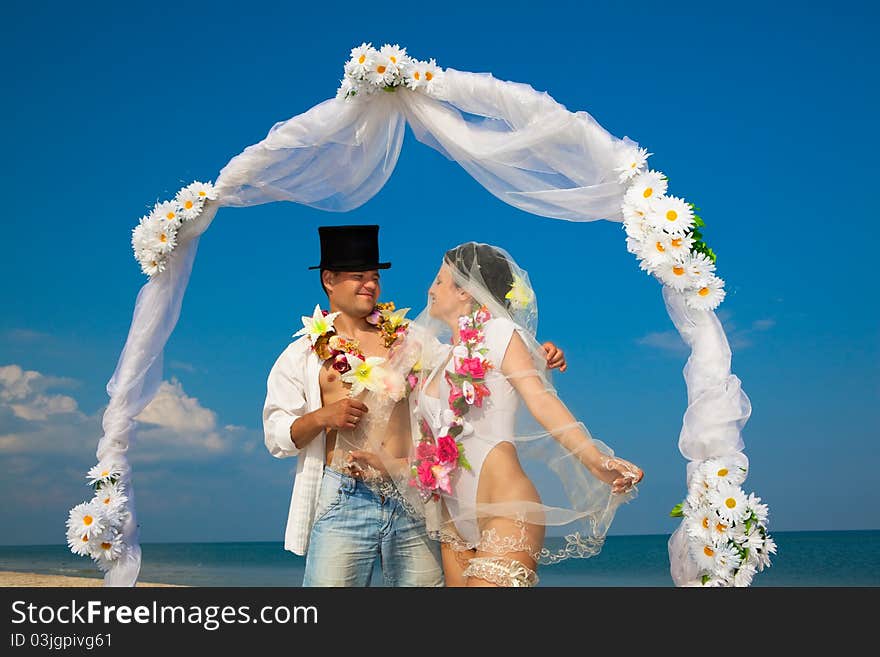 Groom with bride wearing lei, standing under archway on beach. Groom with bride wearing lei, standing under archway on beach