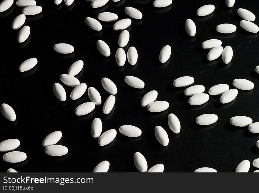 White pills spread out on black surface. White pills spread out on black surface