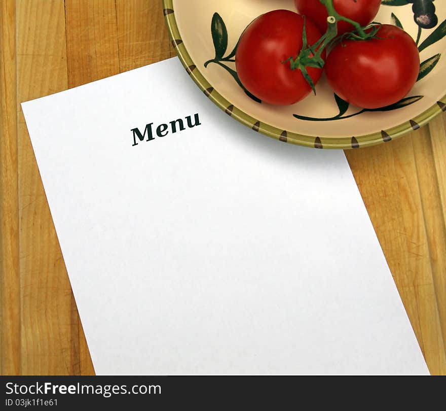 The word Menu on white paper with copy space, on cutting board with decorative bowl filled with tomatoes.