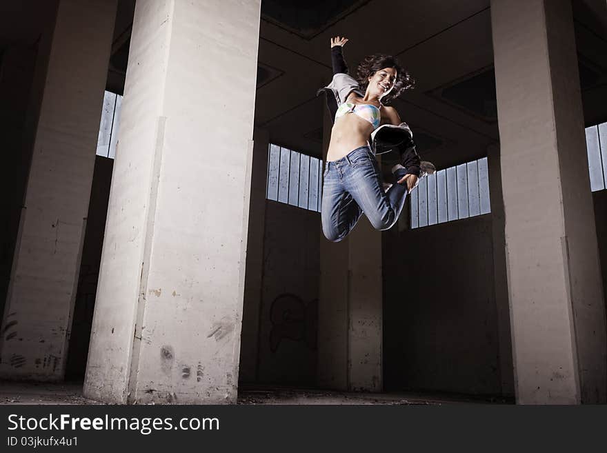 Smiling hip hop dancer girl jumping high with legs up in old grungy factory hall. Smiling hip hop dancer girl jumping high with legs up in old grungy factory hall.