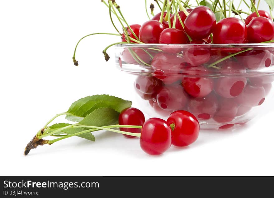 A cherry with a branch lies near a dish with a cherry