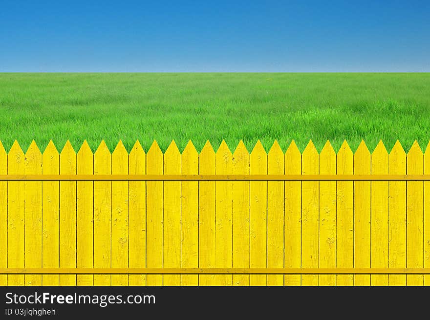 Yellow fence with grass on clear blue sky